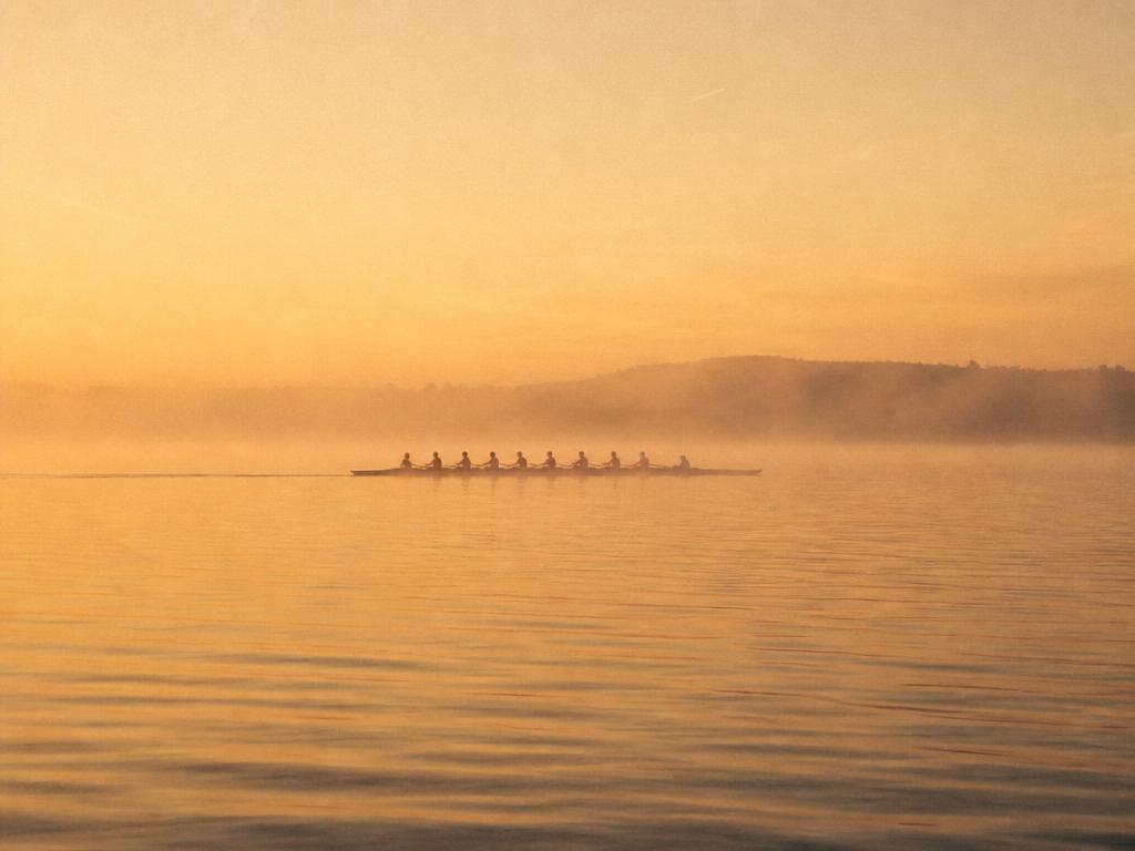 Crew rowing together at dawn, representing team coaching partnership